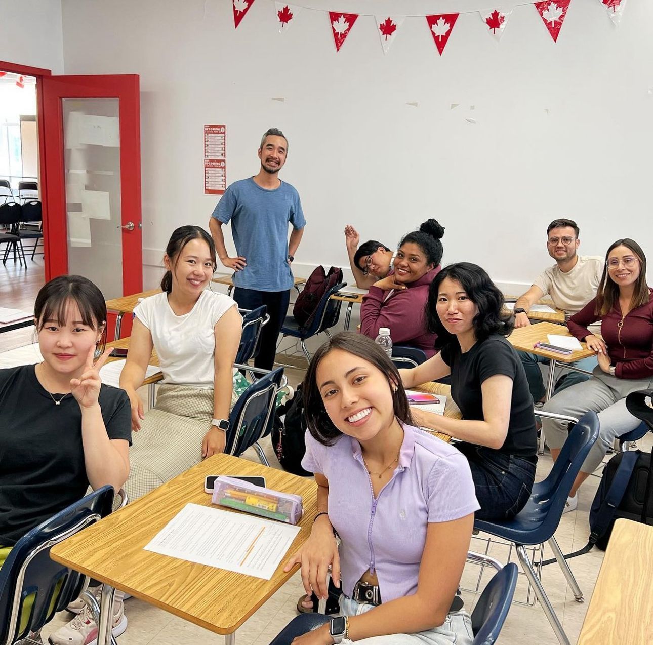 Smiling students and instructor in a classroom decorated with Canadian flags.