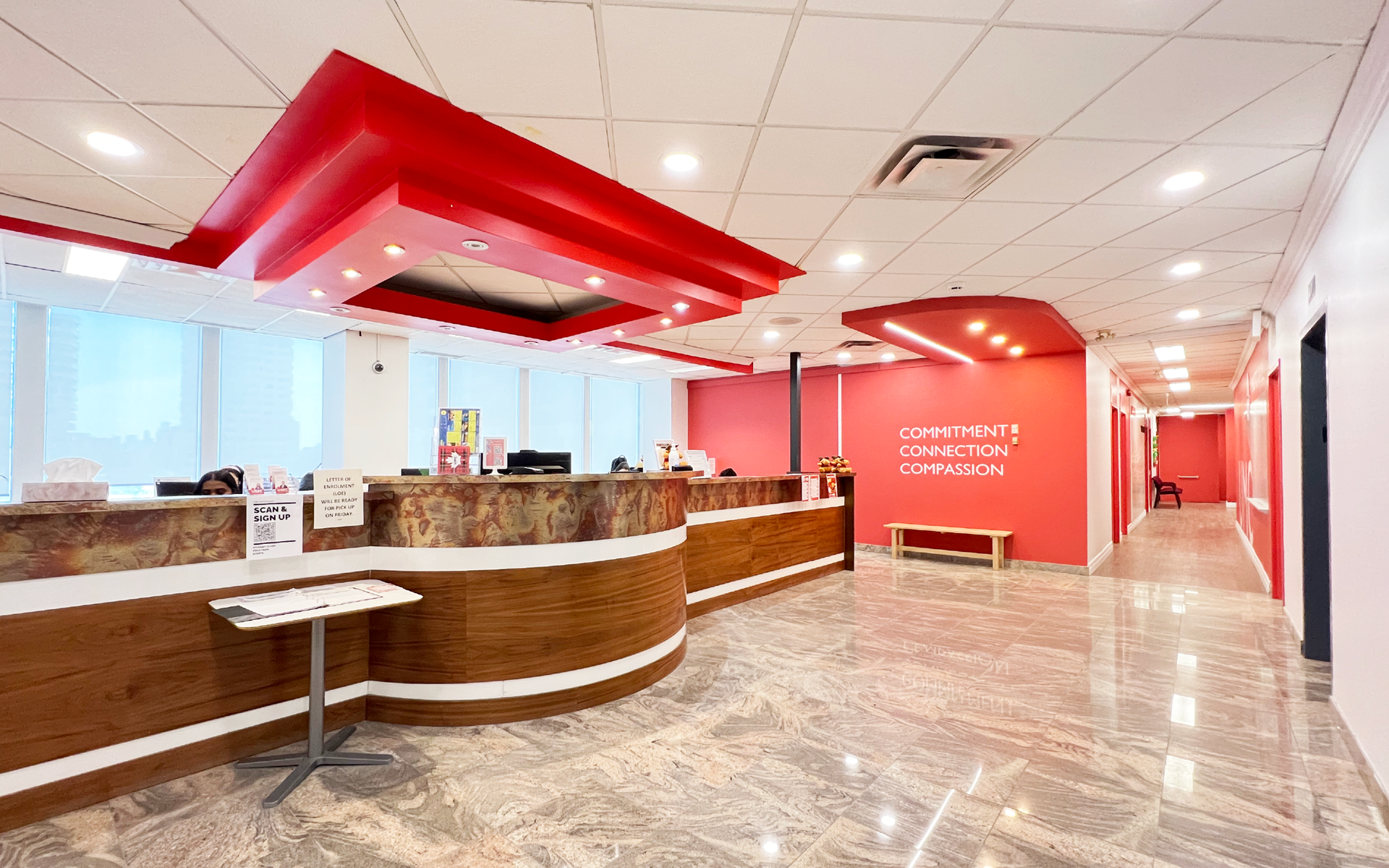 Reception area with red and pink accents. Marble floor, curved reception desk, waiting area, and hallway.
