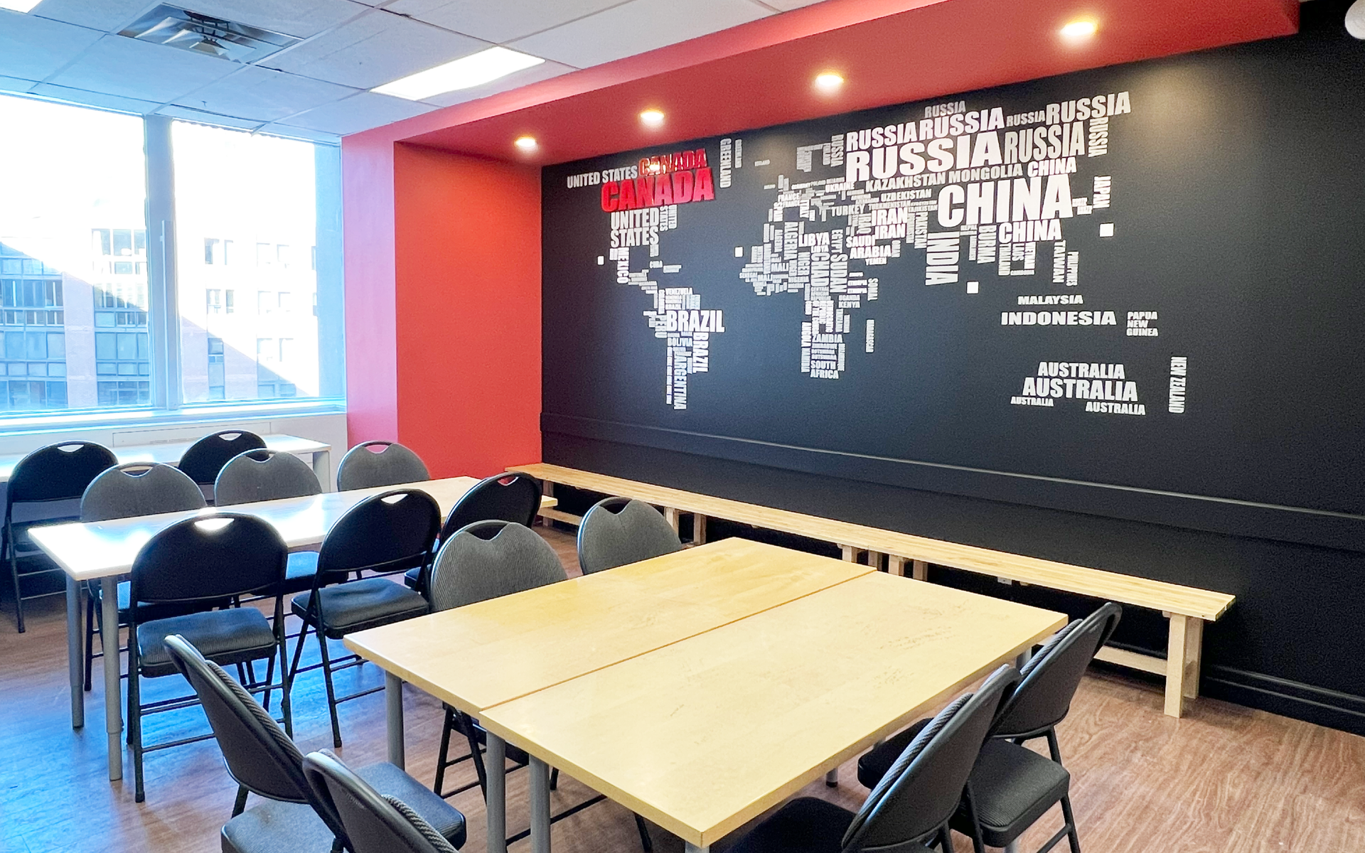 Classroom with tables, chairs, and a world map painted on a black wall. Red and white accents.