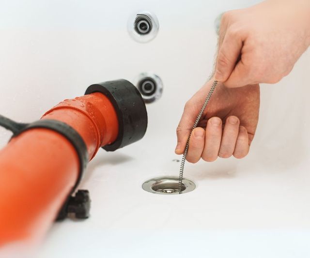 A person is using a drain cleaner to clean a drain in a bathtub.