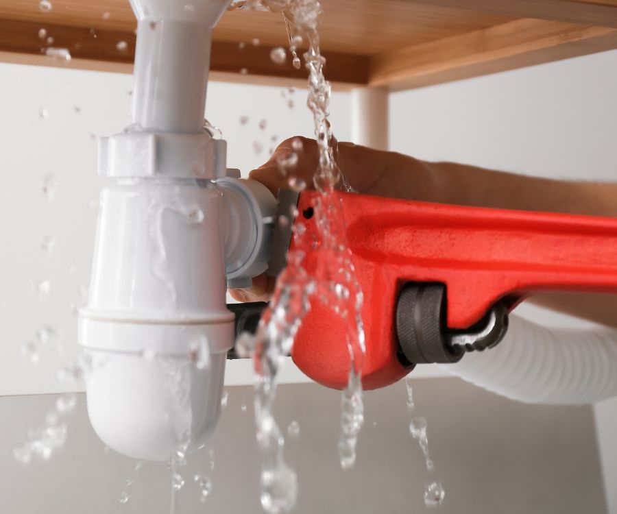A person is fixing a leaking sink pipe with a wrench.