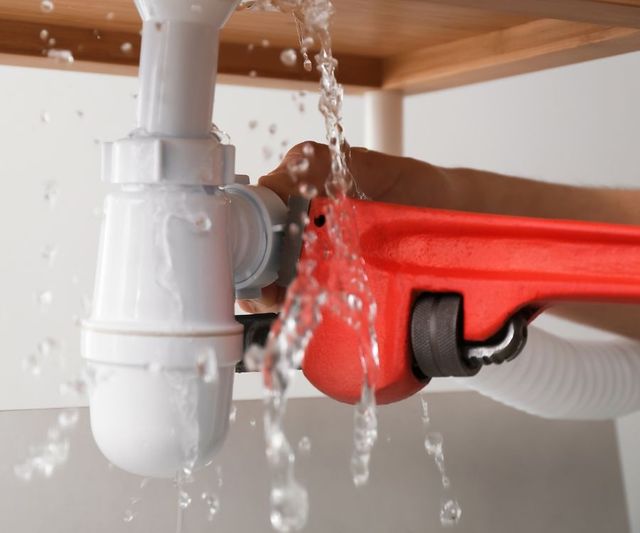 A person is fixing a leaking sink pipe with a wrench.