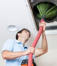 A man is cleaning an air vent with a broom.