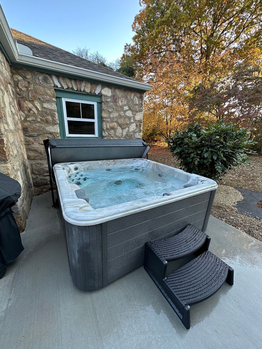 Hot tub with bubbling water on a concrete patio next to a stone building with a small window.