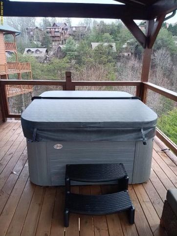 Hot tub on a wooden deck with a forest and houses in the background. A black step stool sits in front.