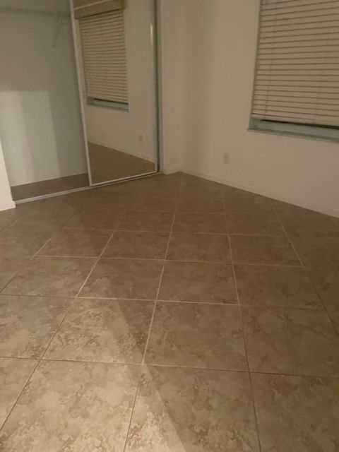 Empty room with tan tile floor, a large mirror, and a window with blinds.