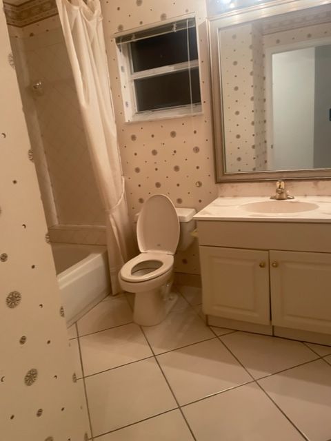 Bathroom with toilet, sink, mirror, bathtub, and patterned wallpaper. Beige and white tones.