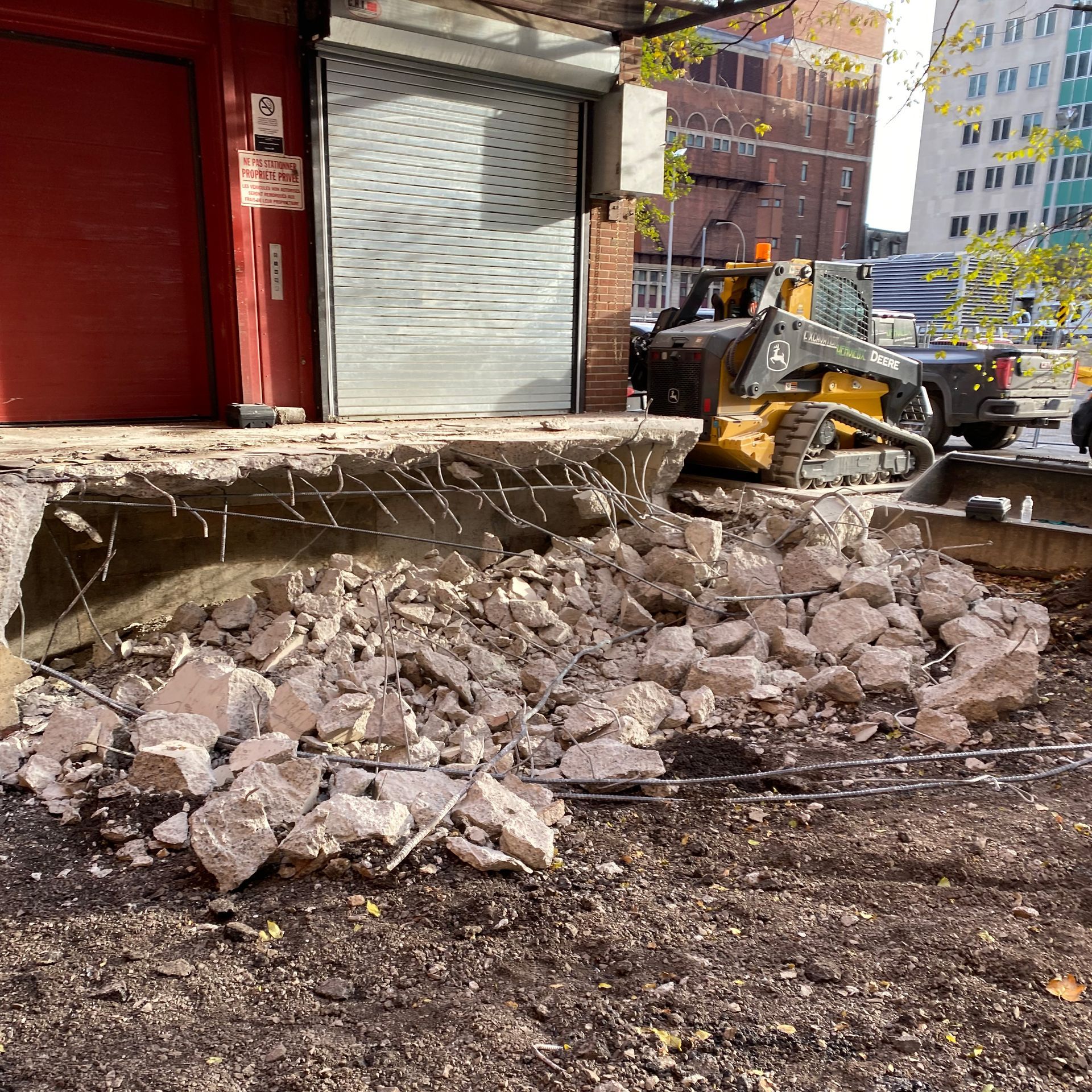 Une équipe de construction utilise une chargeuse compacte pour dégager les gravats et les débris de l'entrée en béton démolie d'un bâtiment.