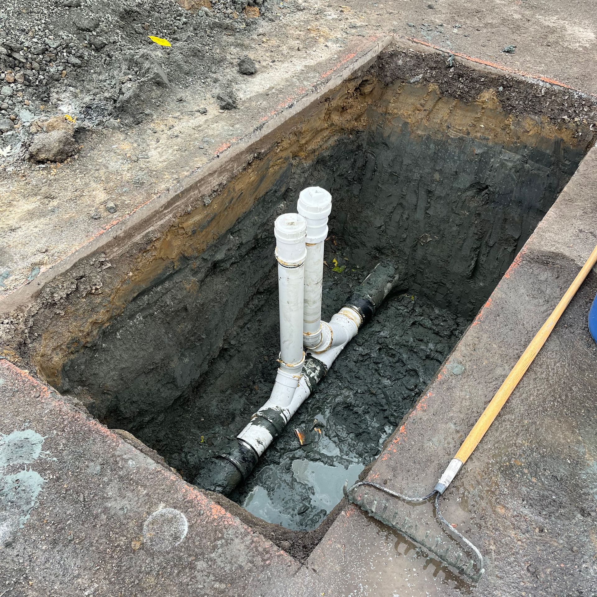 Un ensemble de tuyaux en plastique blanc en forme de T, installé dans une tranchée de terre ouverte sur un chantier de construction.