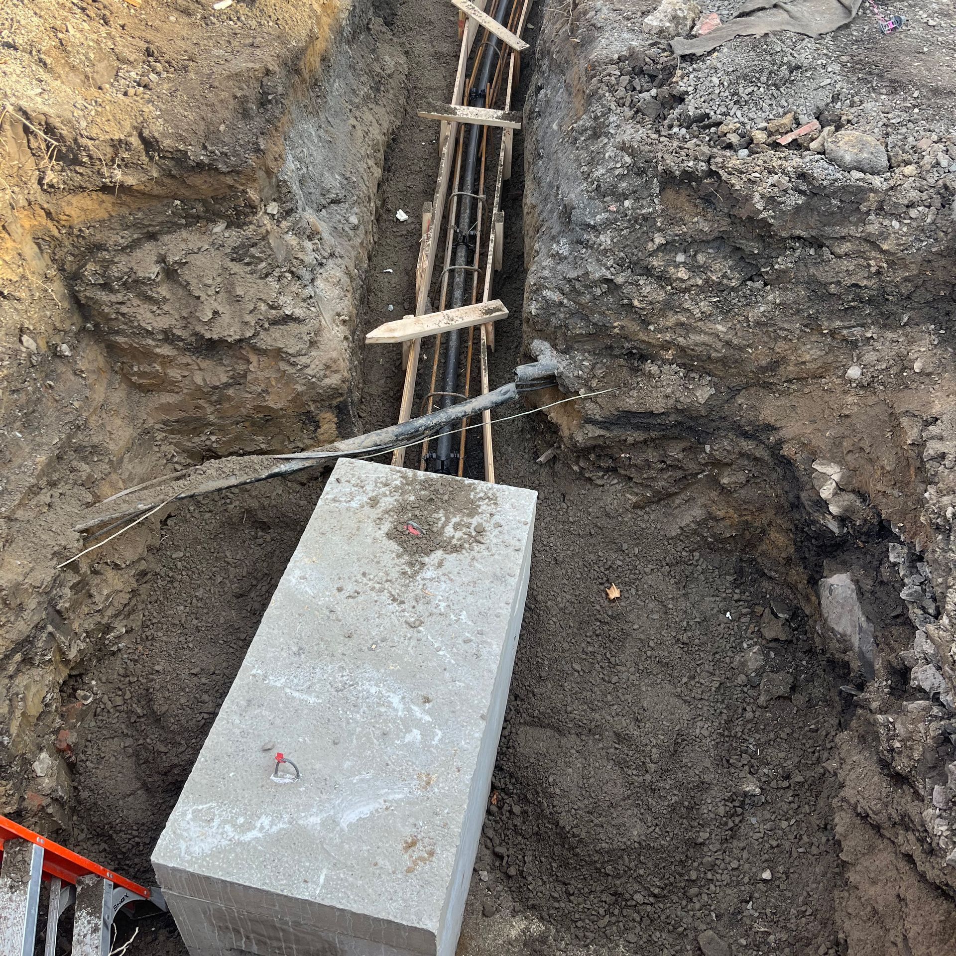 Un chantier de construction montrant un bloc de fondation en béton dans une tranchée excavée avec une armature en acier.