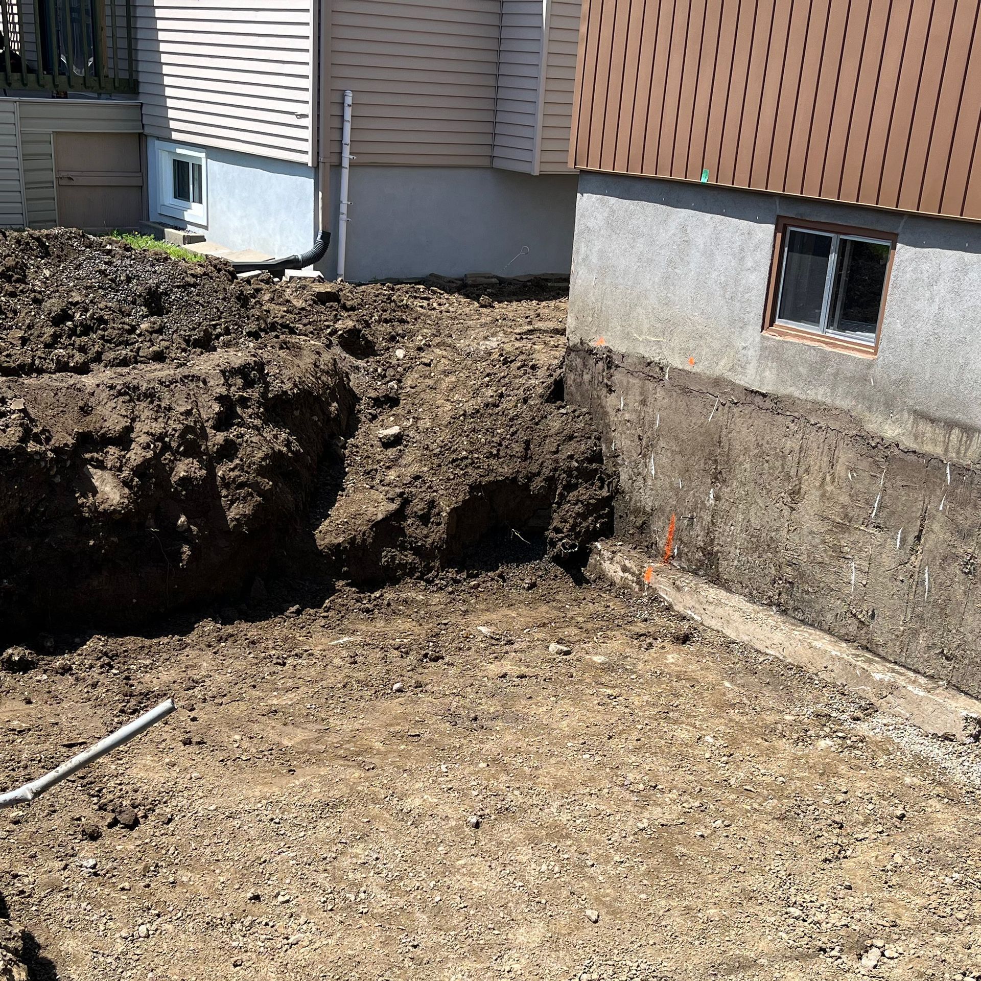 Zone de terre excavée contre les fondations en béton et le mur extérieur d'une maison d'habitation.