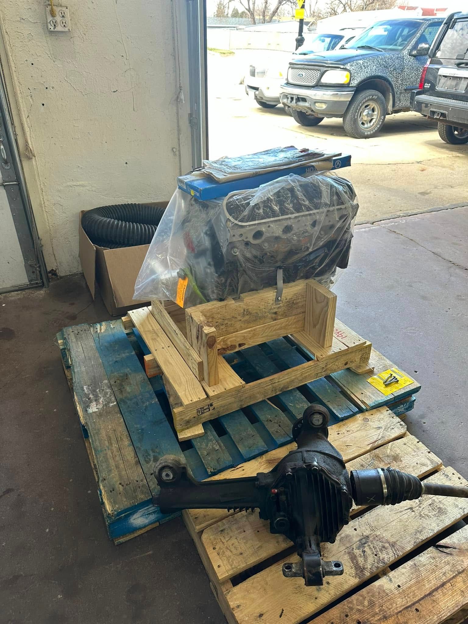 Wrapped motorized equipment strapped to a wooden pallet on a dolly in an outdoor loading area | MRM Auto LLC