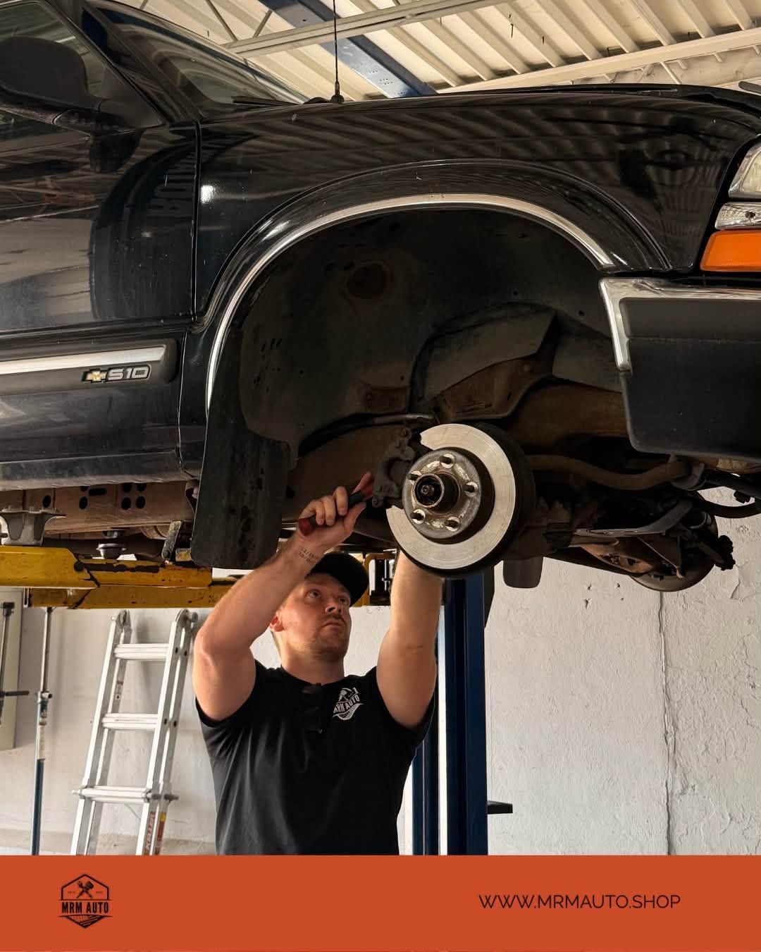 Mechanic inspecting a truck’s front brake and suspension in an auto shop lift | MRM Auto LLC