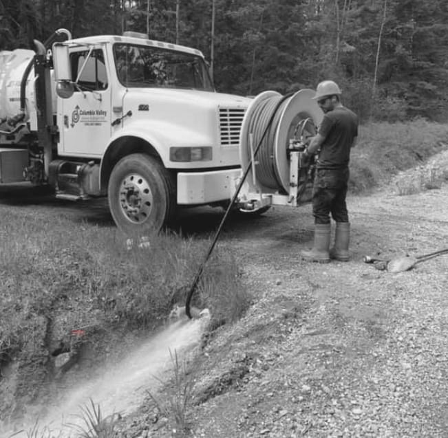 A black and white photo of a man standing next to a vacuum truck