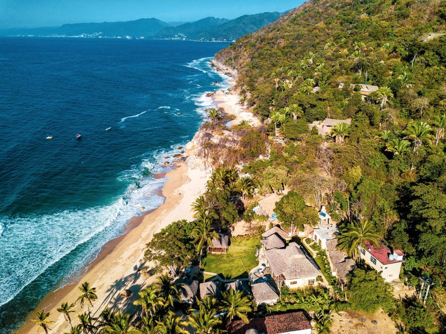 Una vista aérea de una playa rodeada de árboles y montañas.