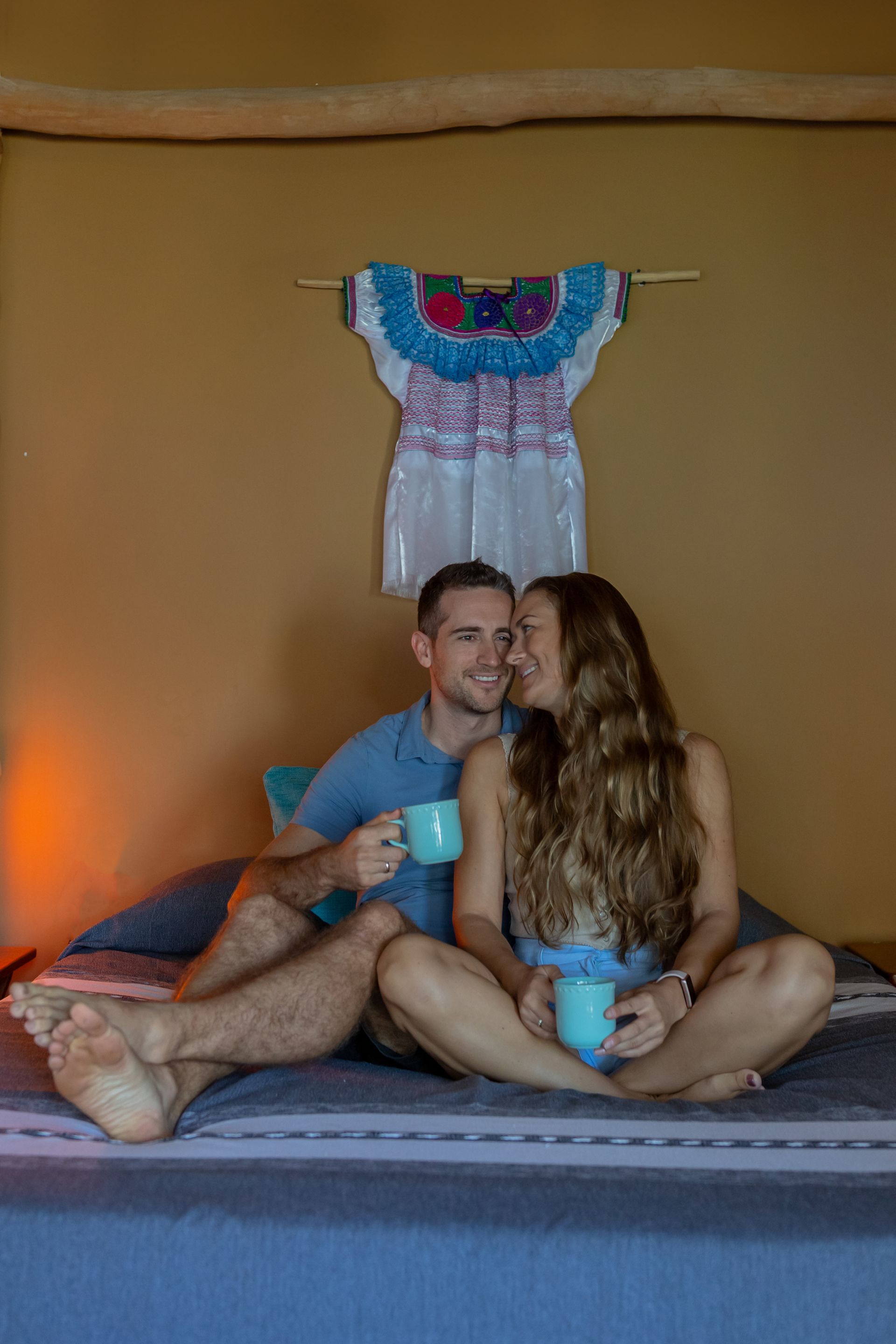 Un hombre y una mujer están sentados en una cama sosteniendo tazas de café.