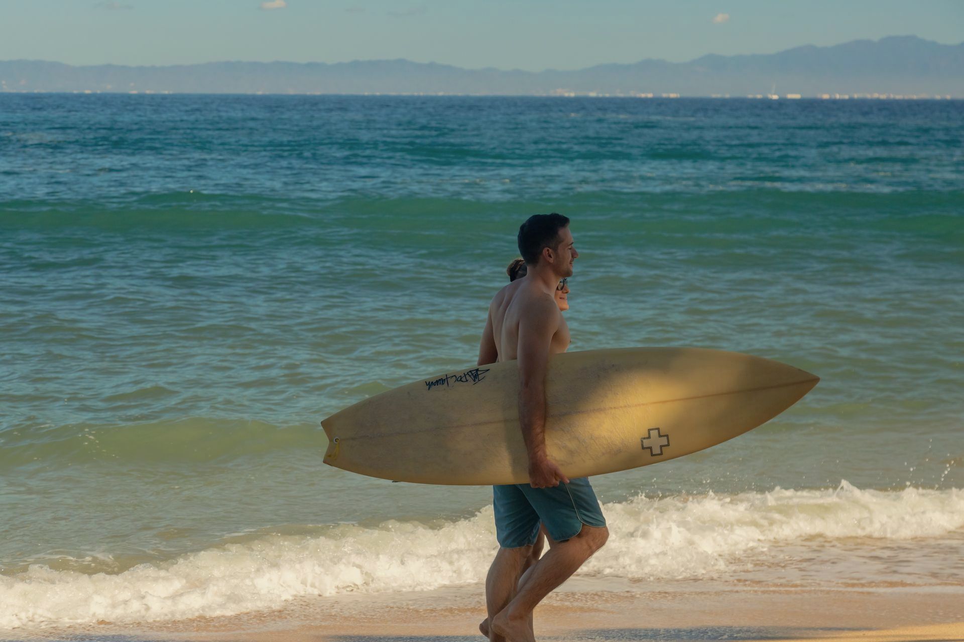 Un hombre lleva una tabla de surf en la playa.