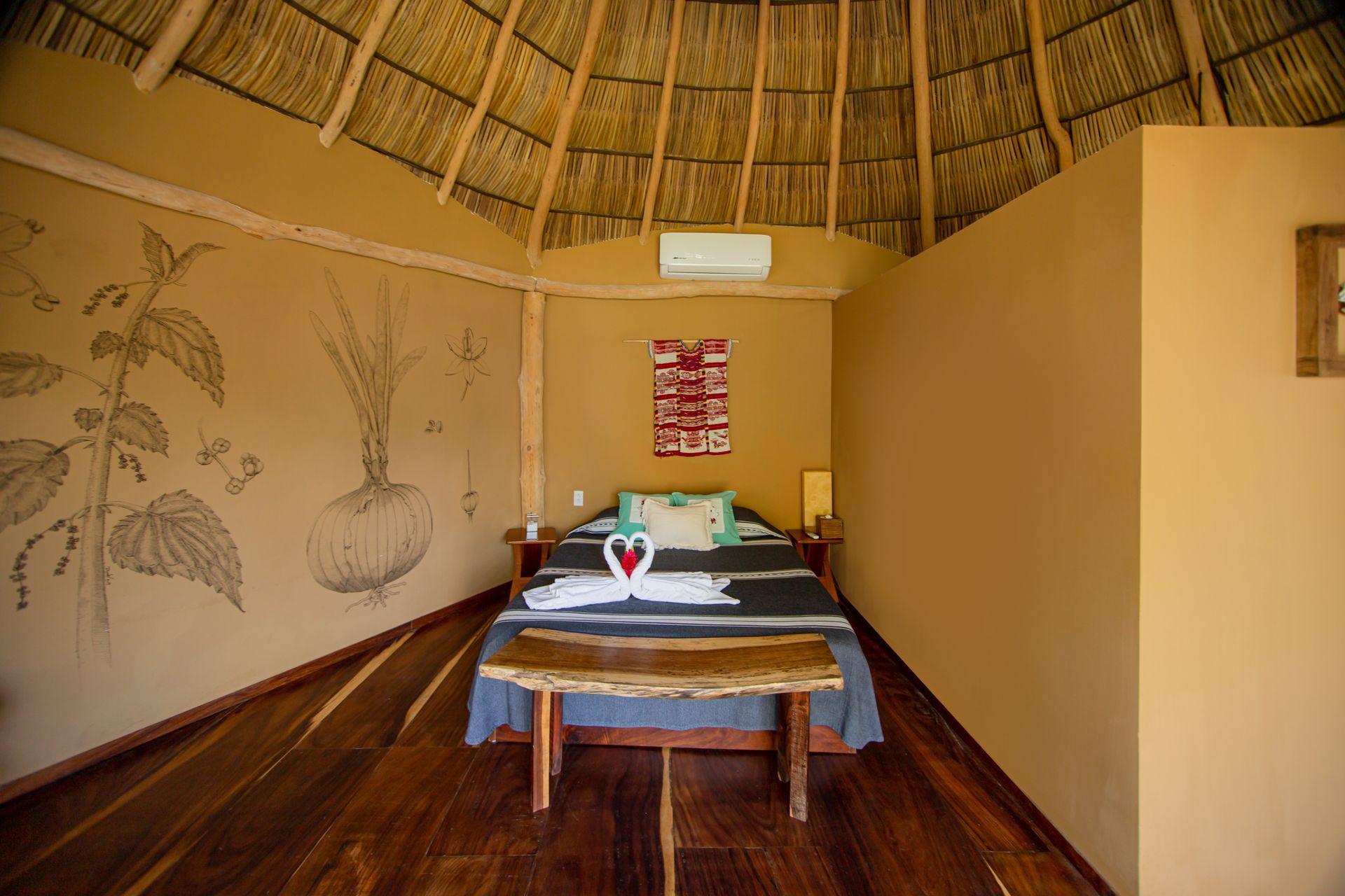 Un dormitorio con cama, banco y techo de paja.