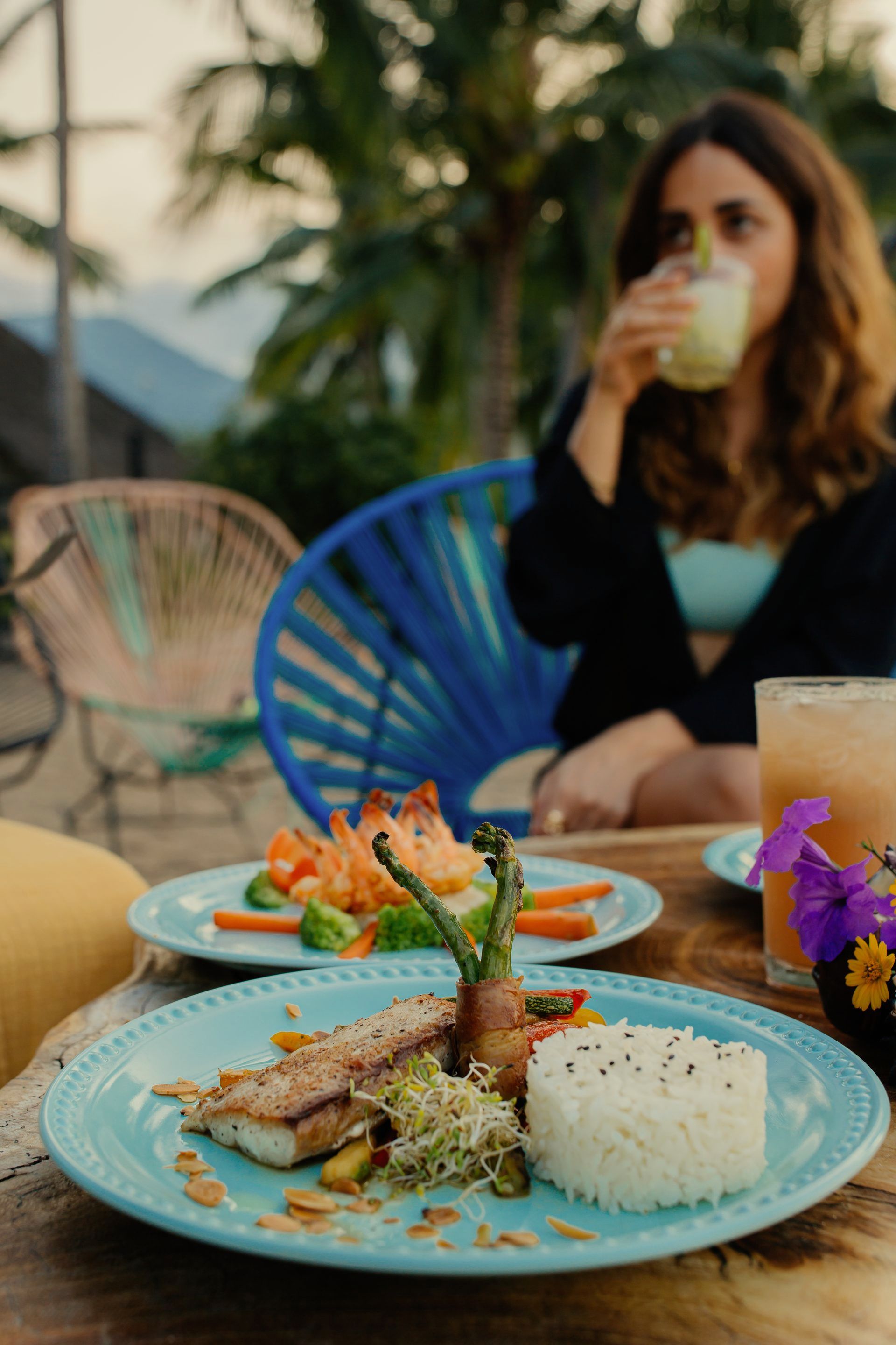 Una mujer está sentada en una mesa con platos de comida y bebidas.