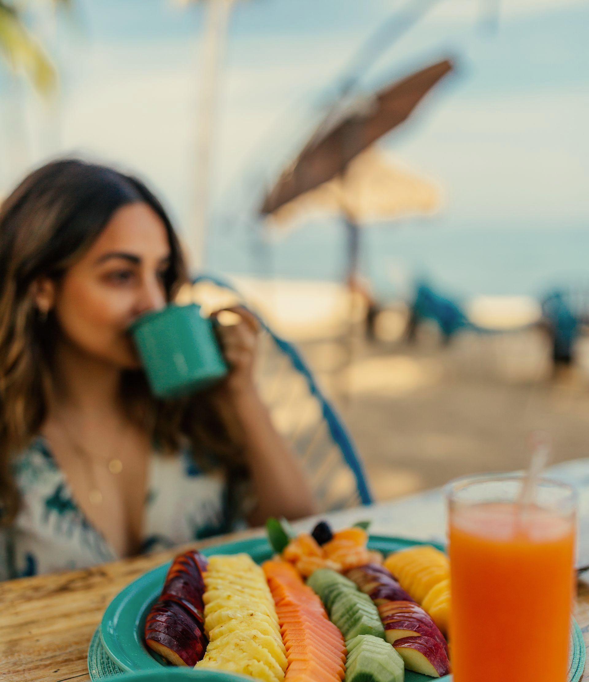Una mujer está sentada en una mesa con un plato de fruta y un vaso de jugo de naranja.