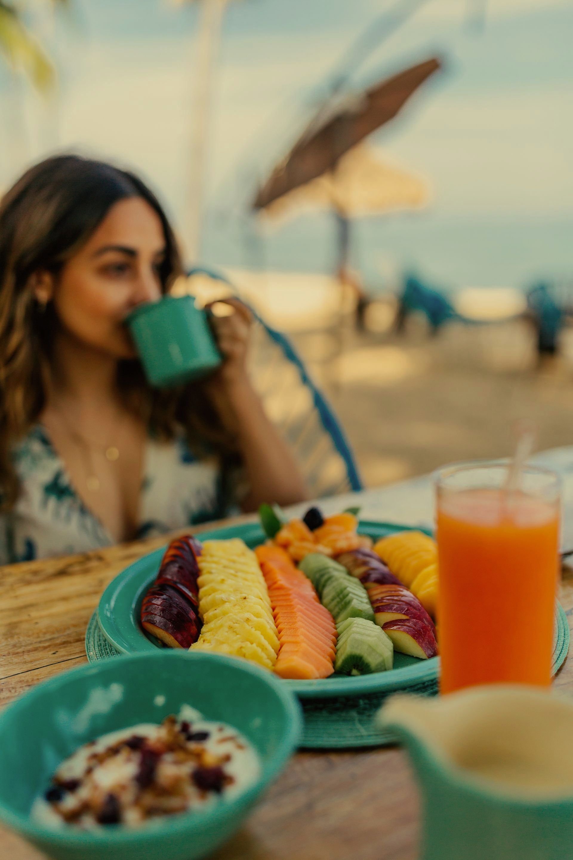Una mujer está sentada en una mesa con un plato de fruta y un vaso de jugo de naranja.