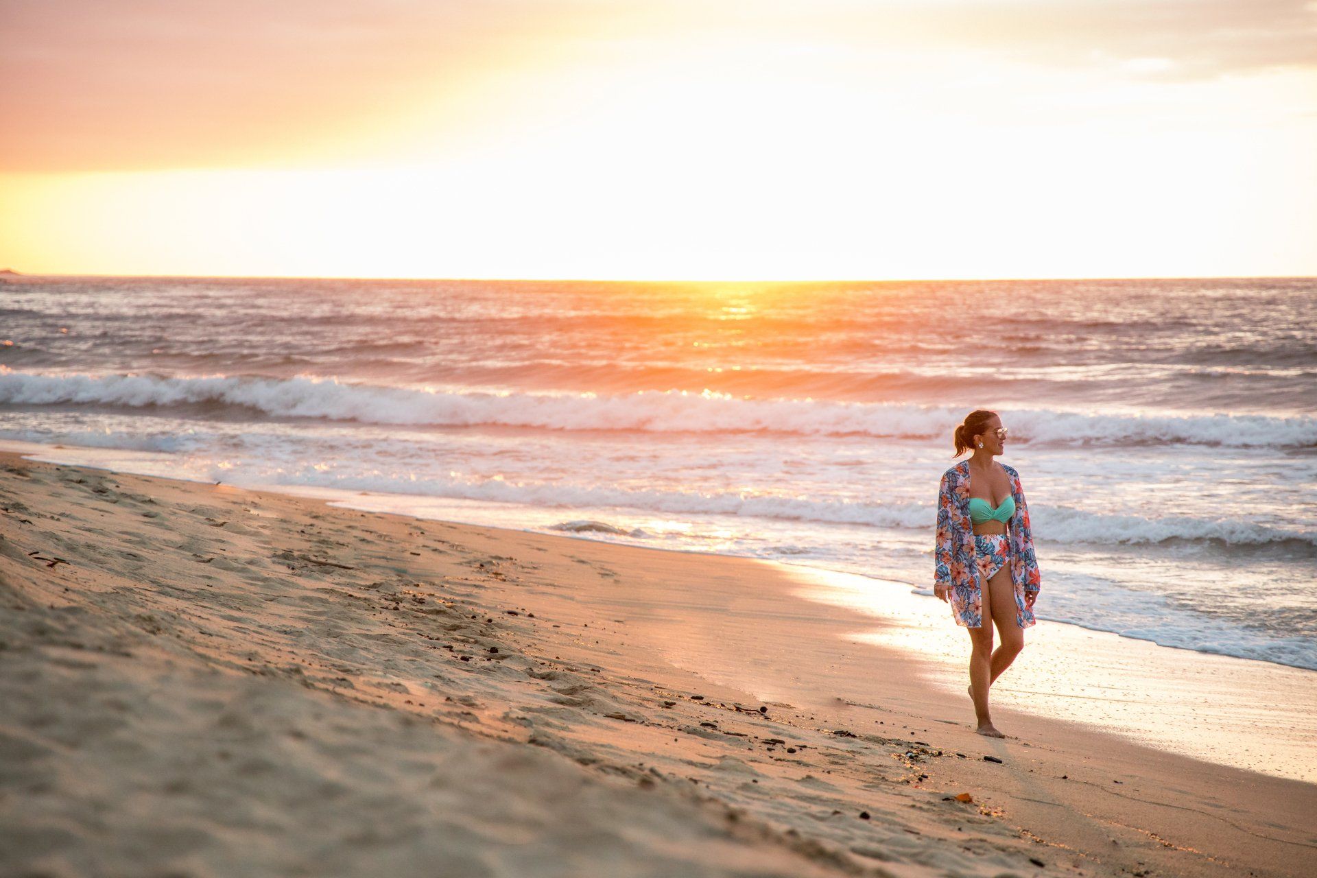 Una mujer camina por la playa al atardecer.