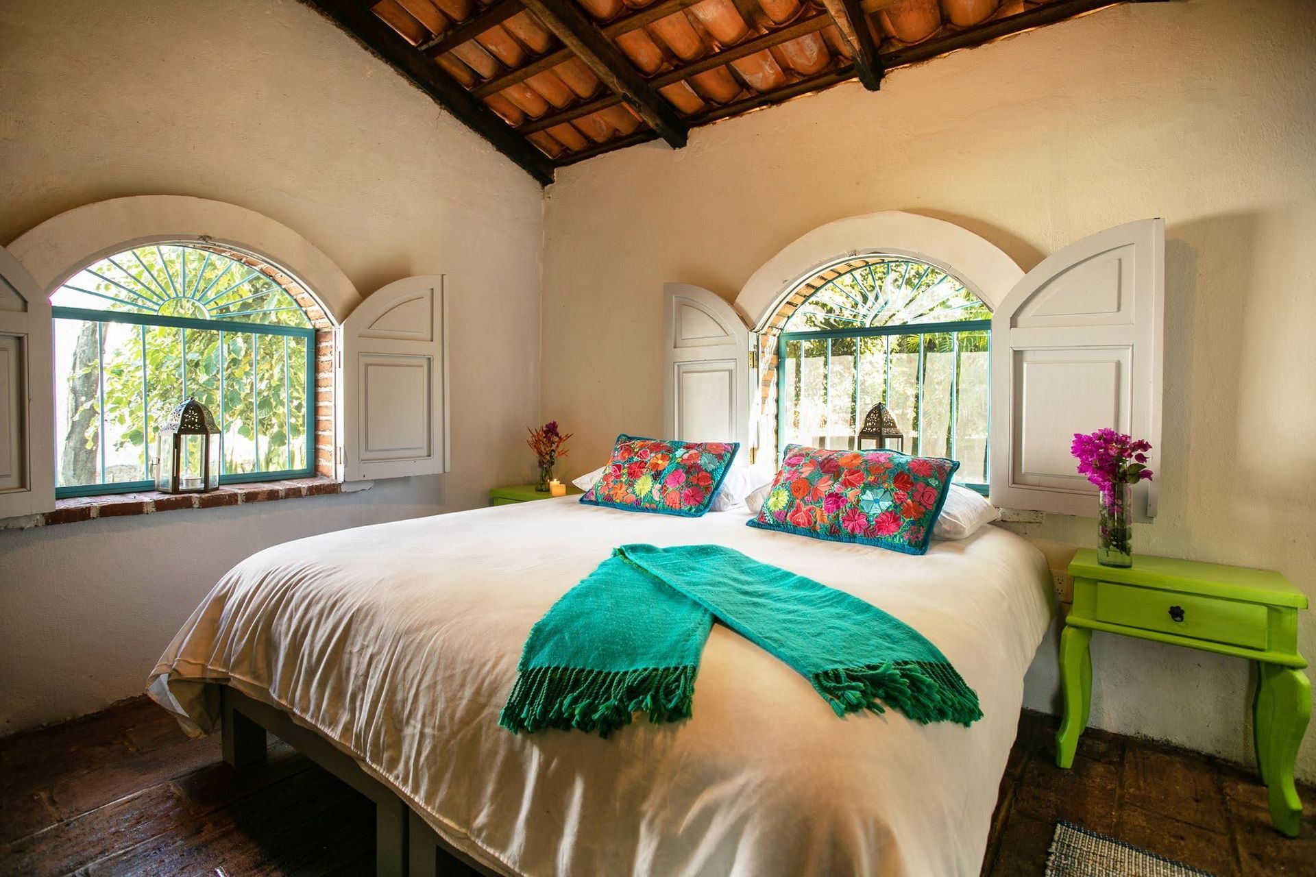 Un dormitorio con una cama, mesita de noche y dos ventanas.
