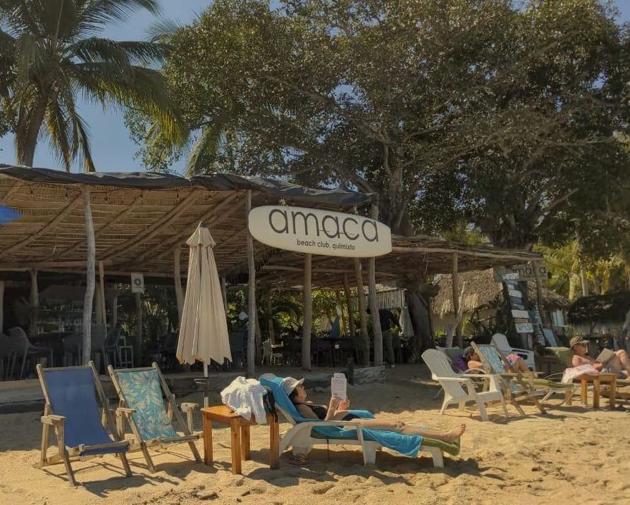 Una playa con sillas y sombrillas y un cartel que dice amaca
