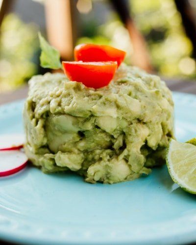 Un plato azul cubierto con guacamole y tomates.