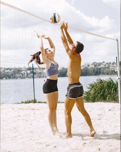 Un hombre y una mujer están jugando voleibol en una playa.