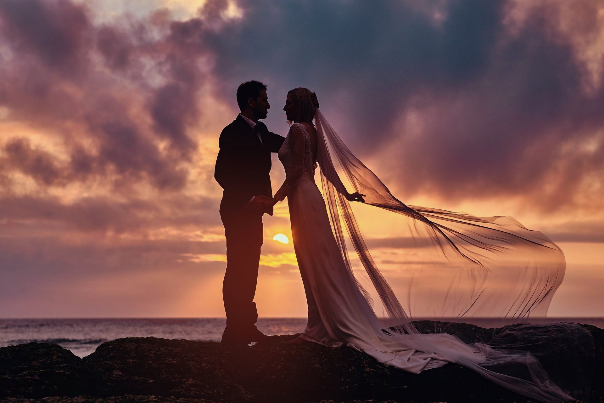 Una novia y un novio están de pie en una playa al atardecer.