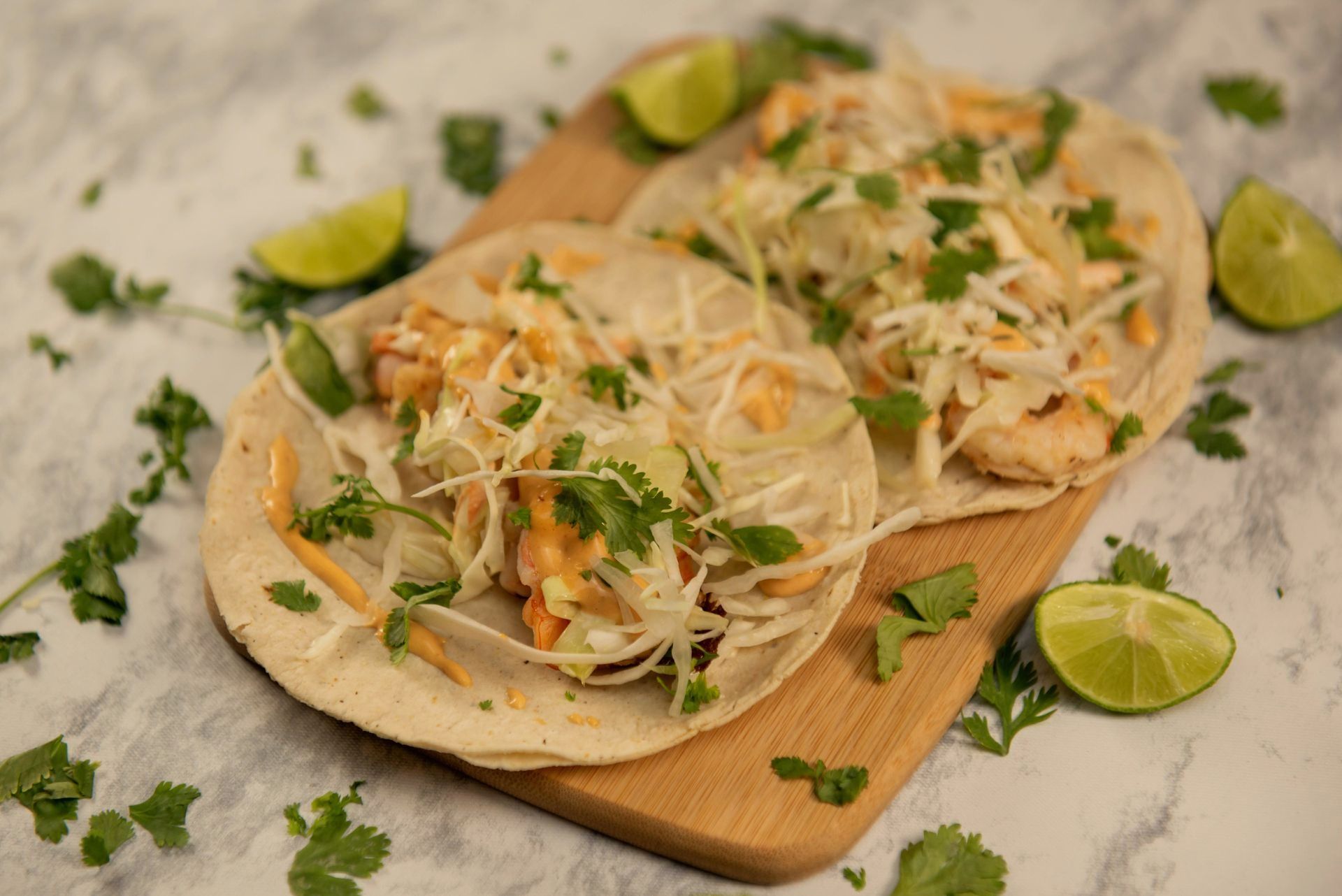 Dos tacos en una tabla de cortar de madera con limones y cilantro.