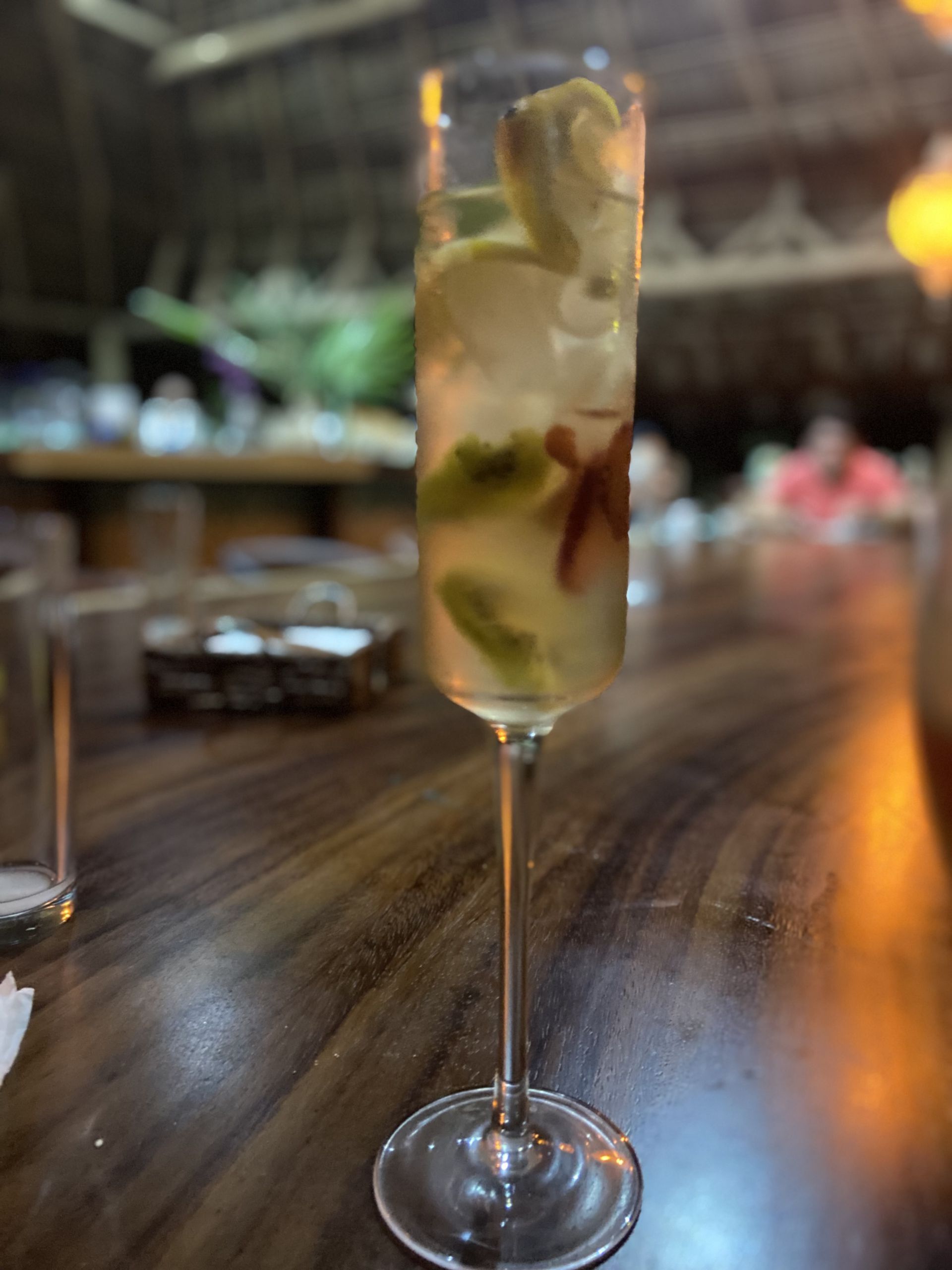 Una copa de vino llena de una bebida está sobre una mesa de madera.