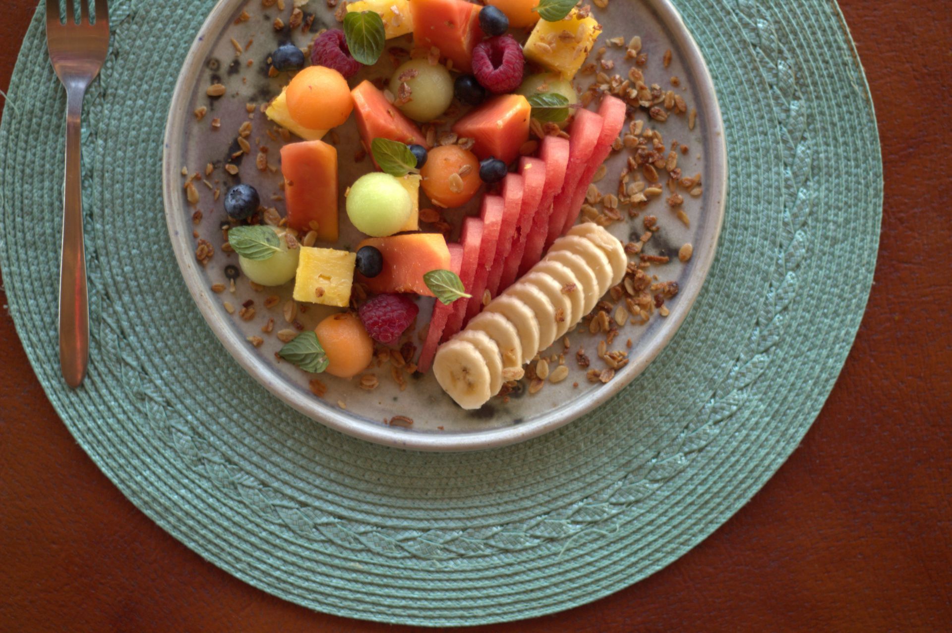 Un plato de fruta sobre un mantel individual con un tenedor.