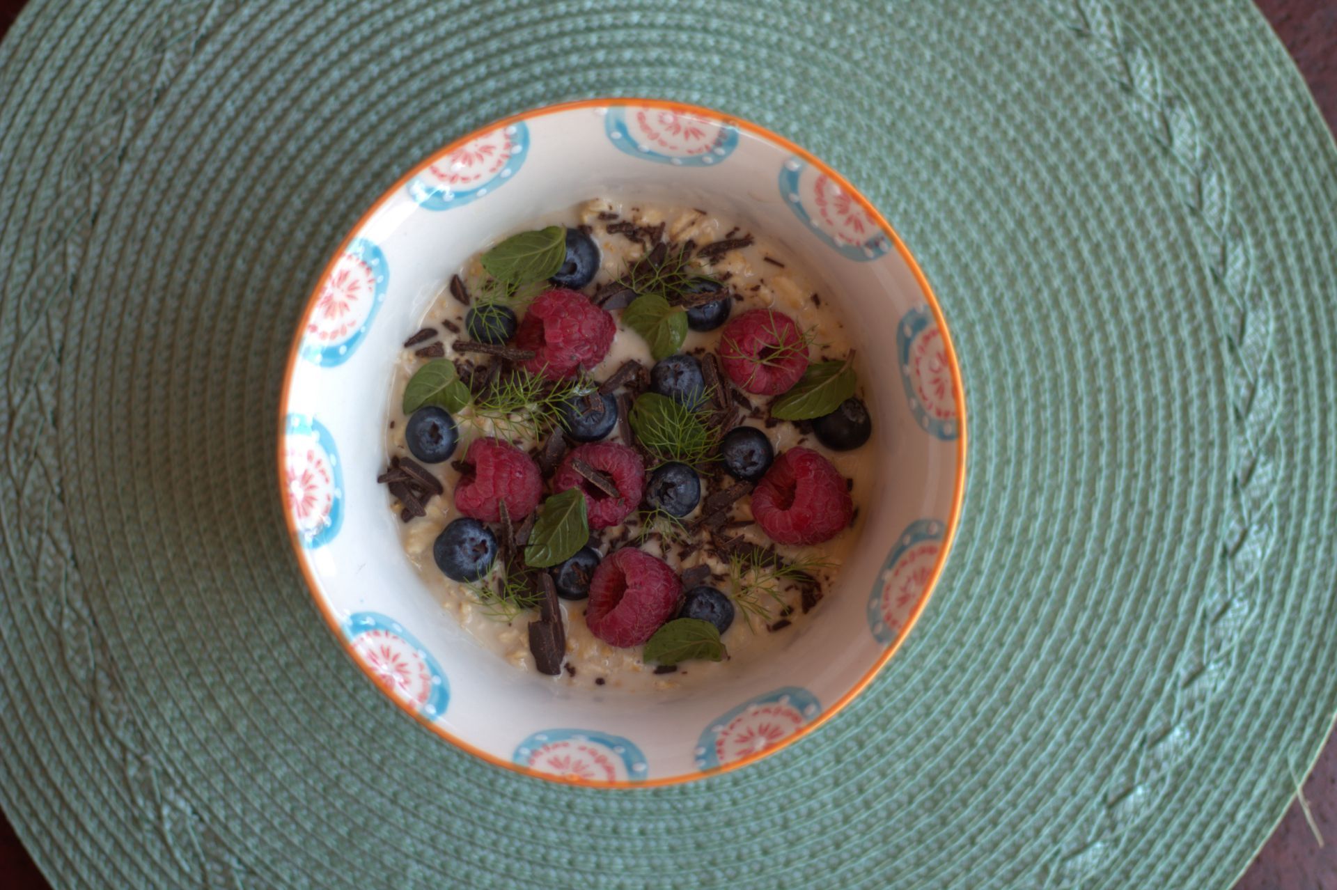 Un tazón de avena con frambuesas, arándanos y menta sobre un mantel verde.