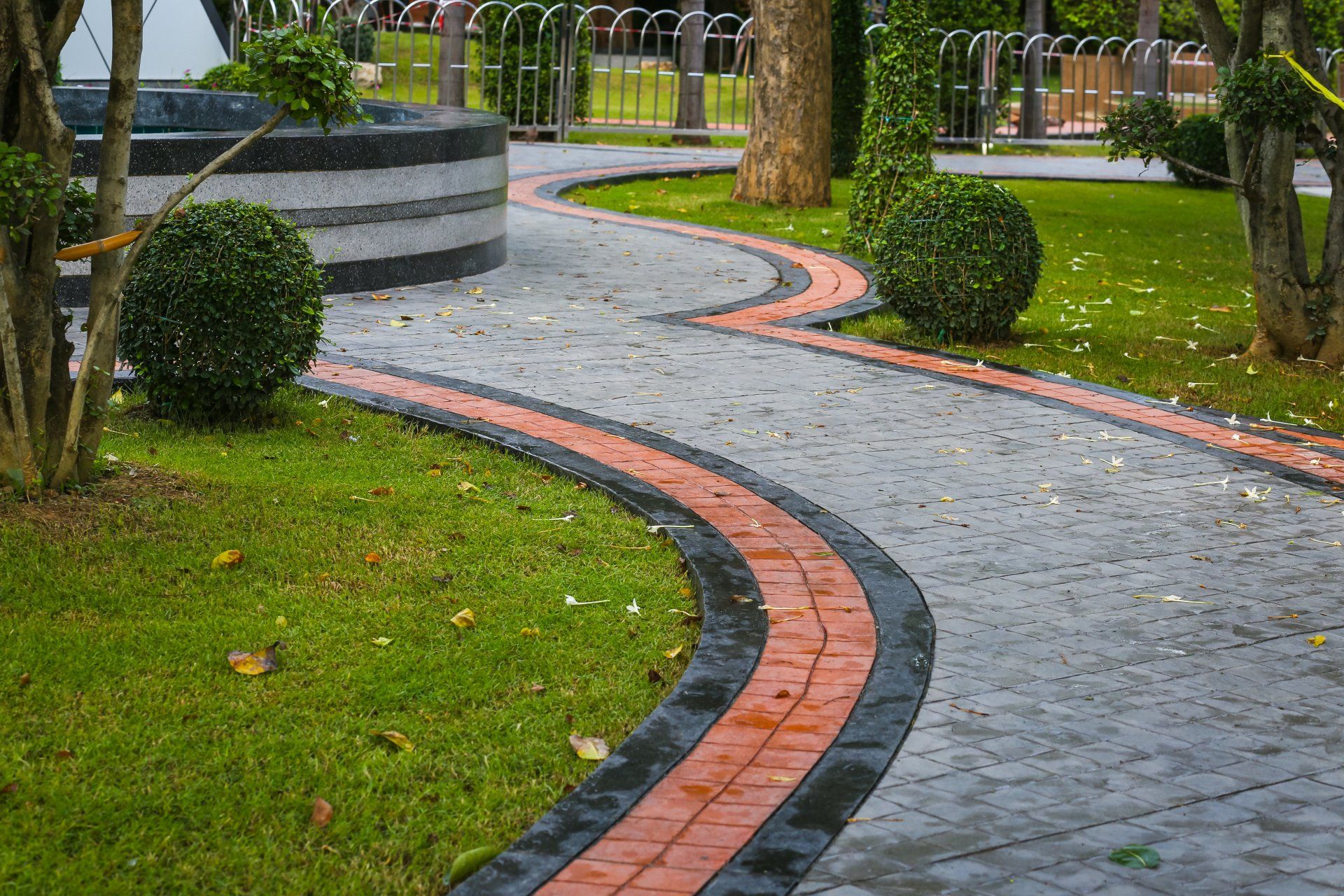 A brick walkway in a park with a fountain in the background.
