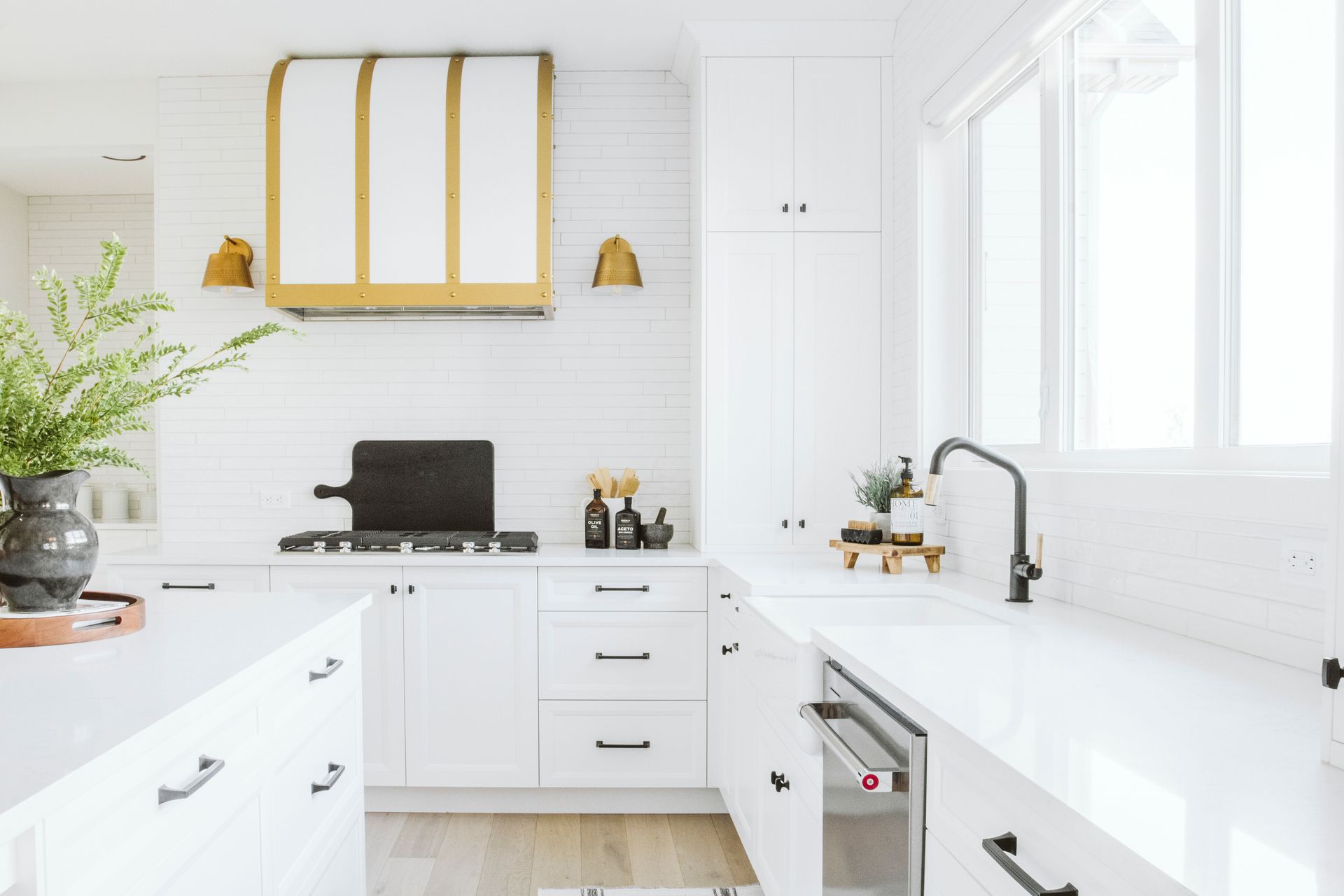 A kitchen with white cabinets , a stove , a sink , and a window.