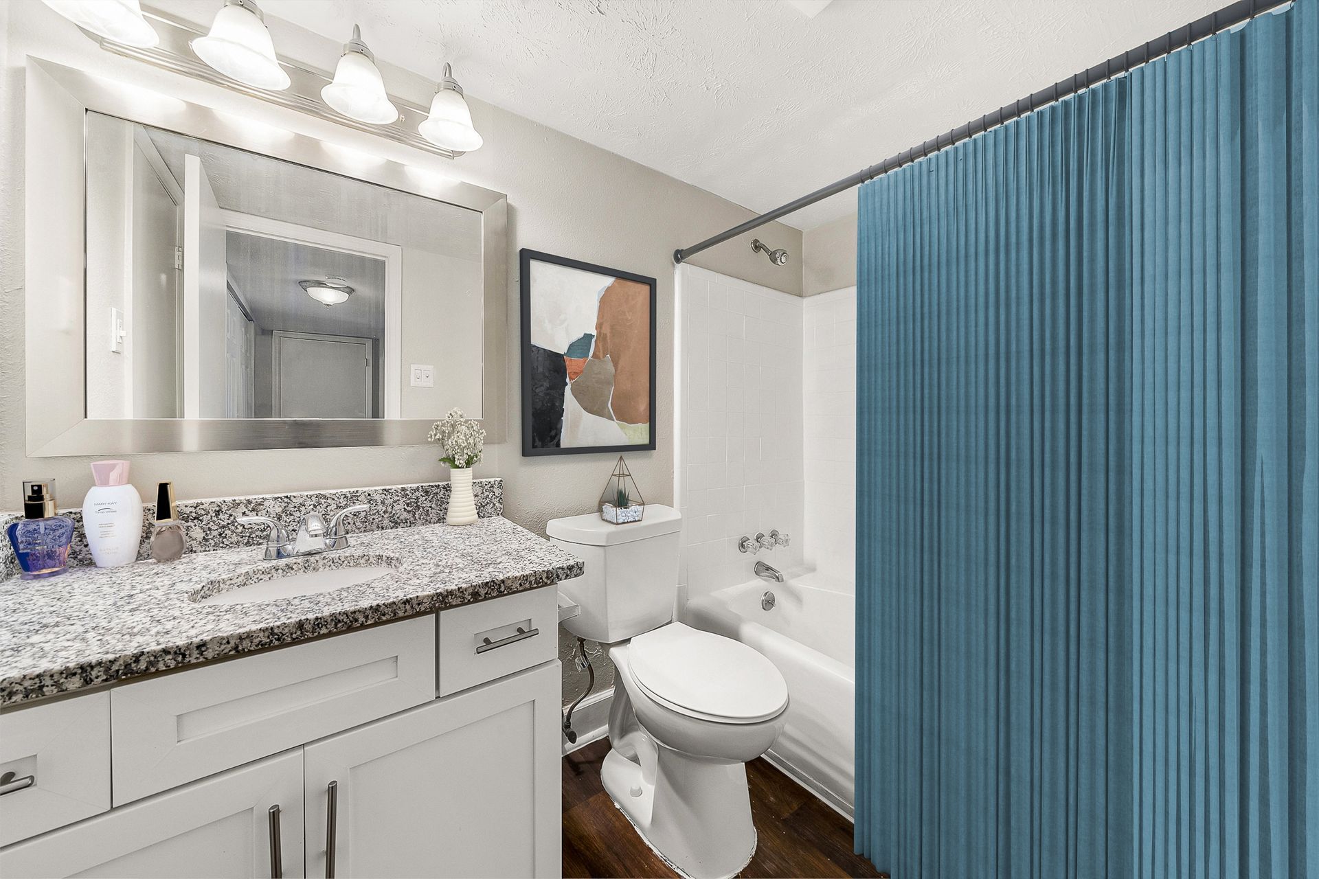 Bright bathroom with granite vanity, mirror lights, toilet, tub, and blue shower curtain