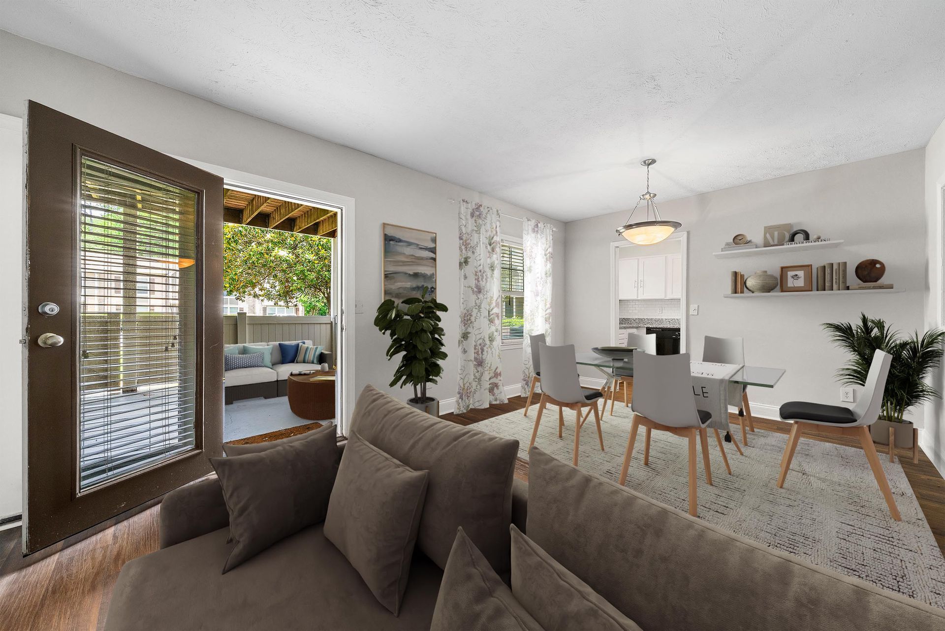 Bright living and dining room with gray sofa, dining table, potted plants, and sliding glass doors to a patio