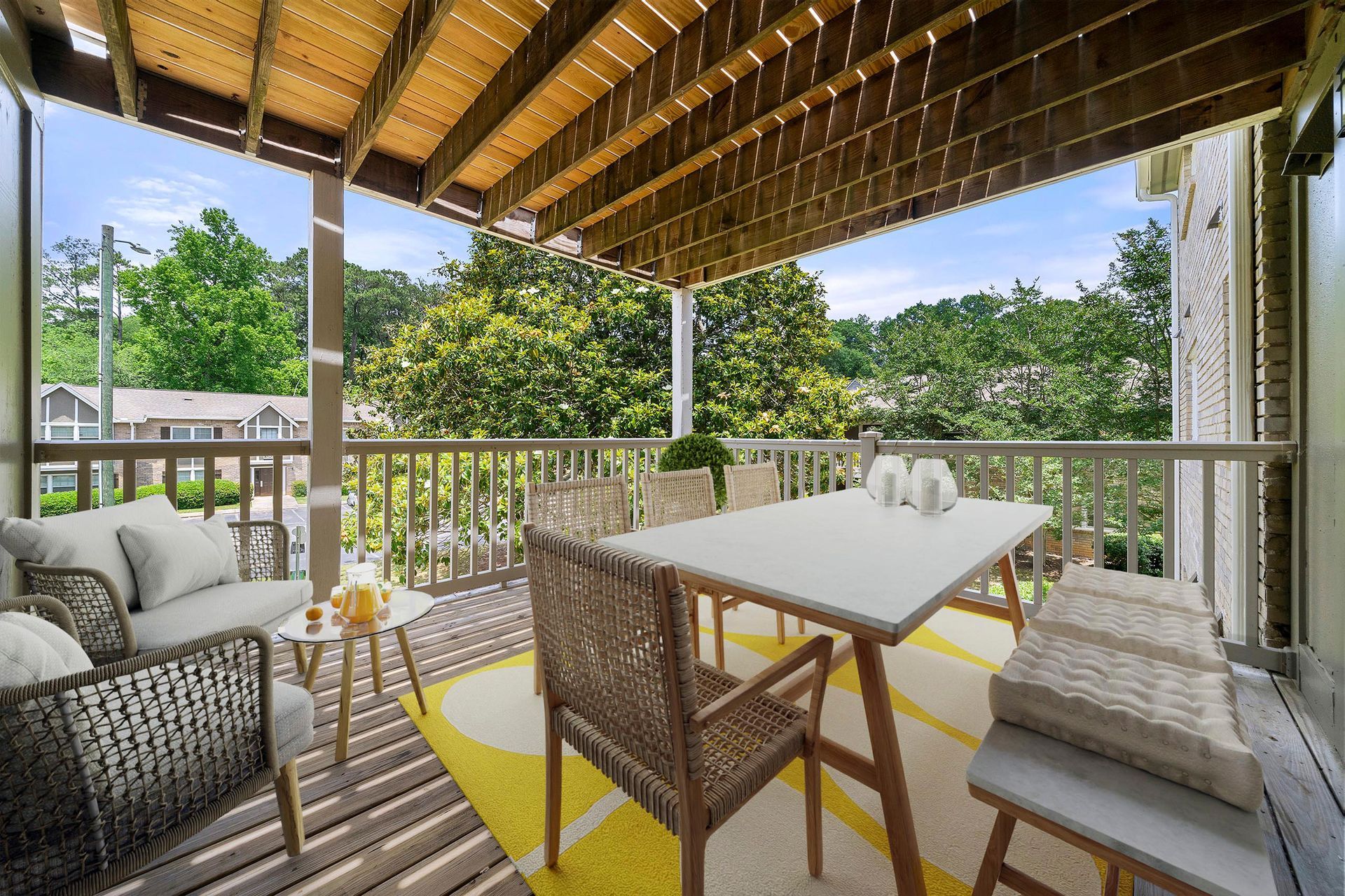 Covered balcony with wicker seating and white table overlooking green trees