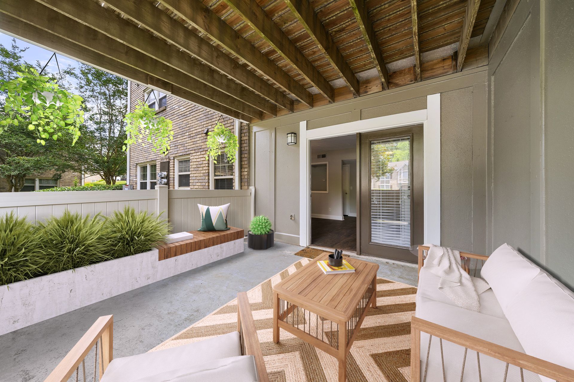 Covered patio with wicker seating, wooden table, potted plants, and sliding glass doors overlooking a yard
