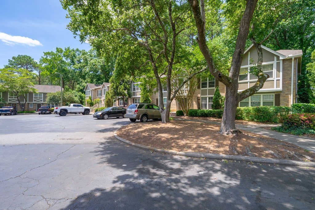 Shaded apartment parking lot with trees, parked cars, and two-story buildings on a sunny day