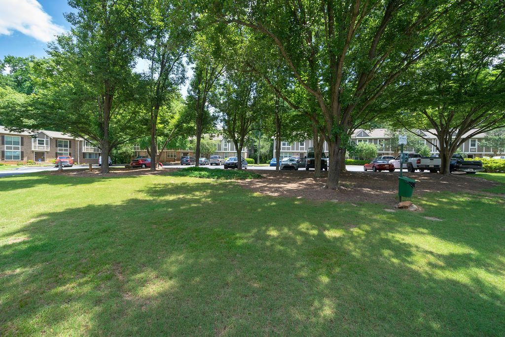 Shady park lawn with large trees, benches, and a building in the background