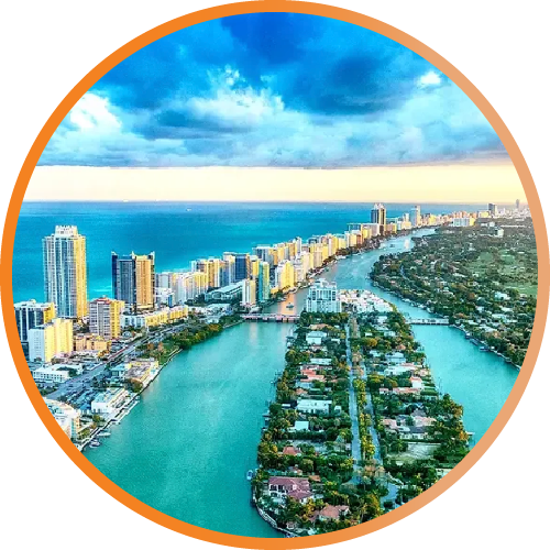 Aerial view of a coastal city with turquoise waterways, high-rise buildings, and a bright blue sky.