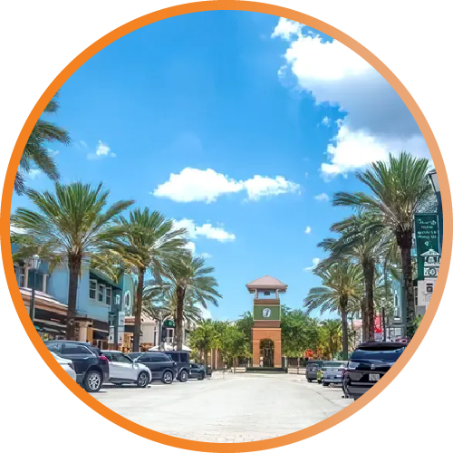 Palm-lined street leading to a clock tower under a bright blue sky, with parked cars on both sides.