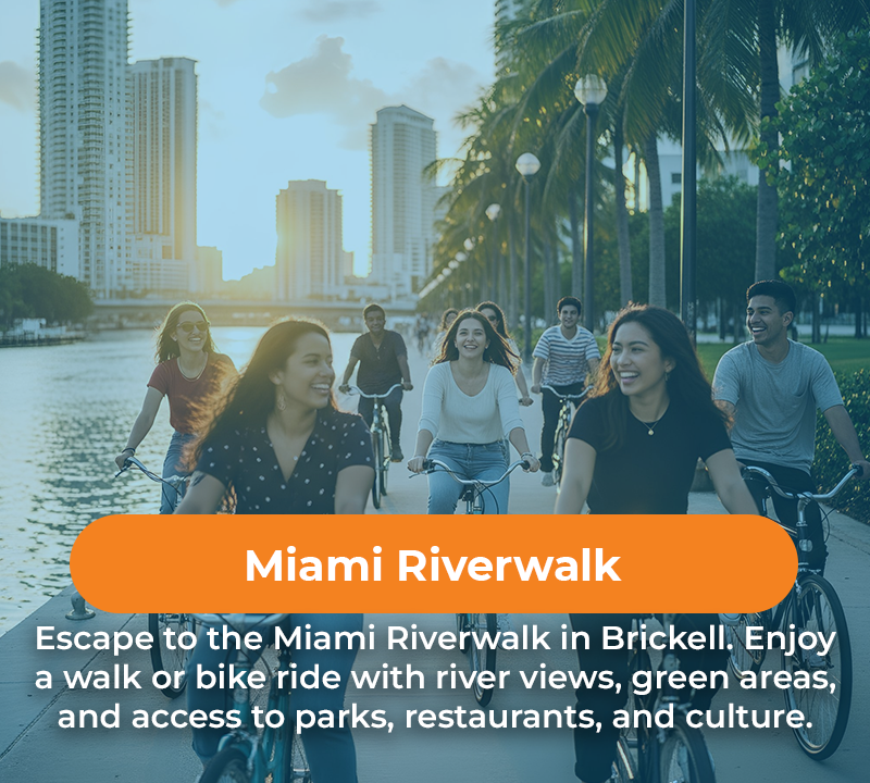 People biking and smiling on the Miami Riverwalk with city and river views.