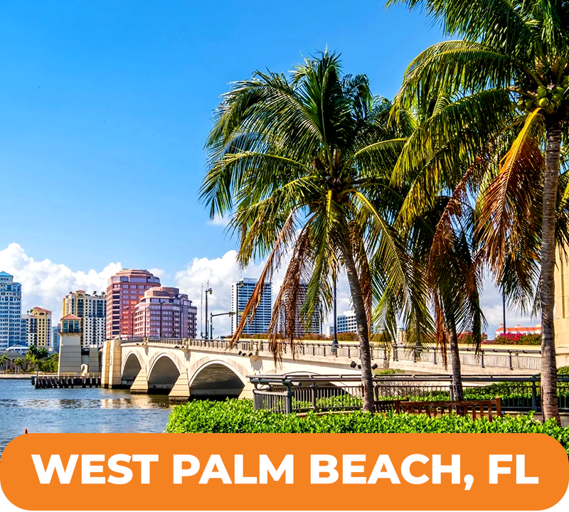 Palm trees frame a bridge in West Palm Beach, Florida, with buildings and blue sky visible.