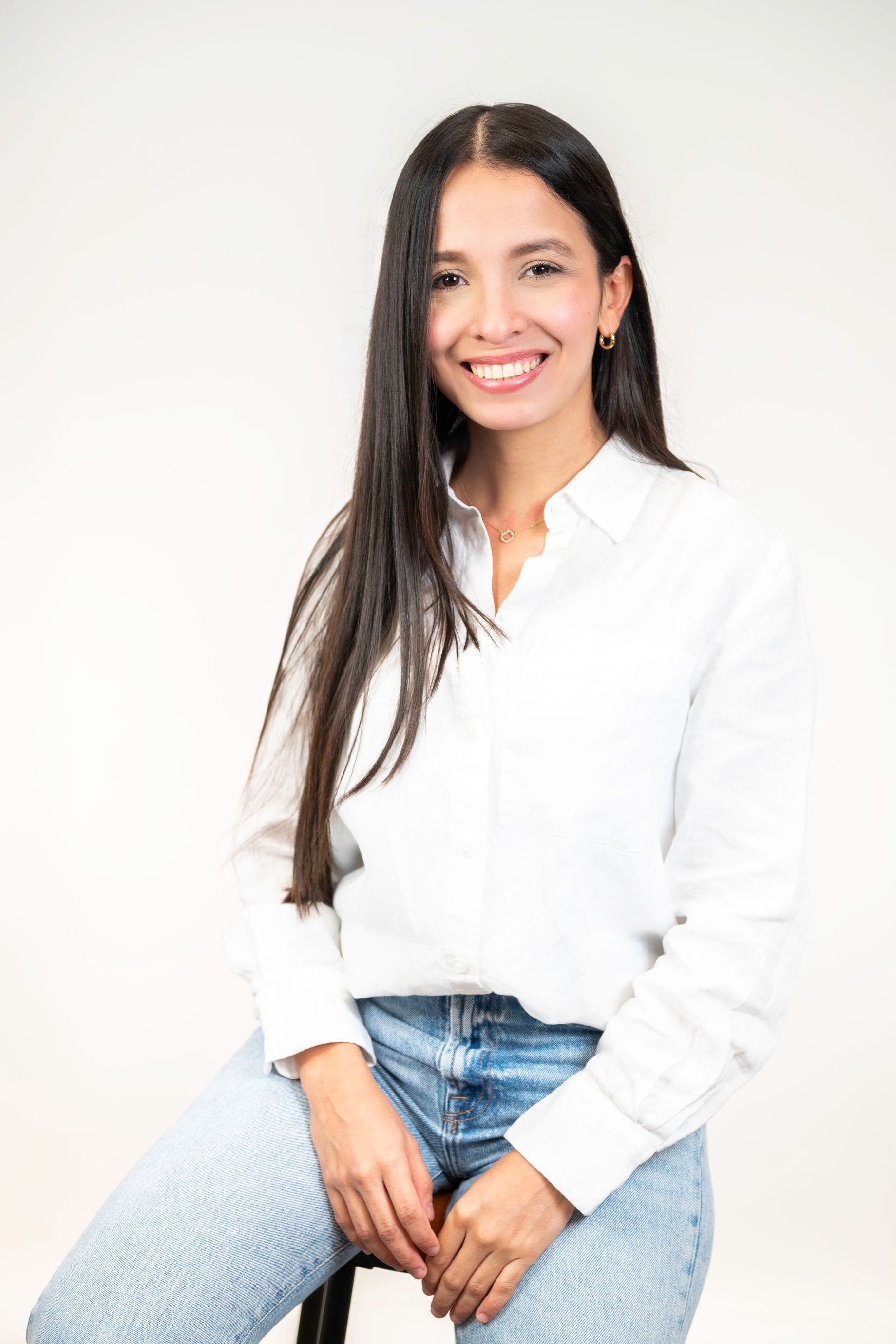 A woman in a white shirt and blue jeans is standing with her arms crossed.