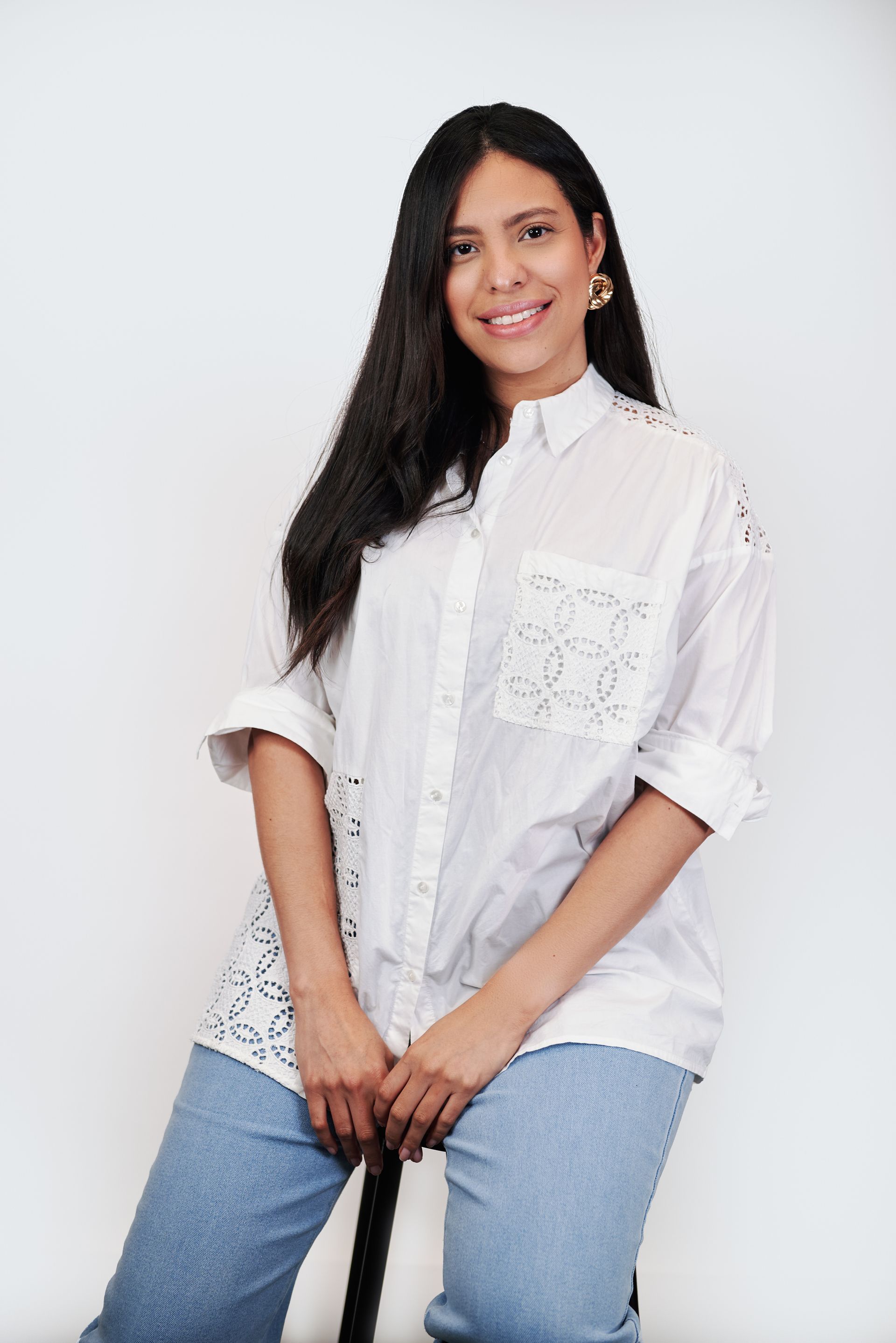 A woman wearing glasses and a white shirt is standing in front of a white wall.