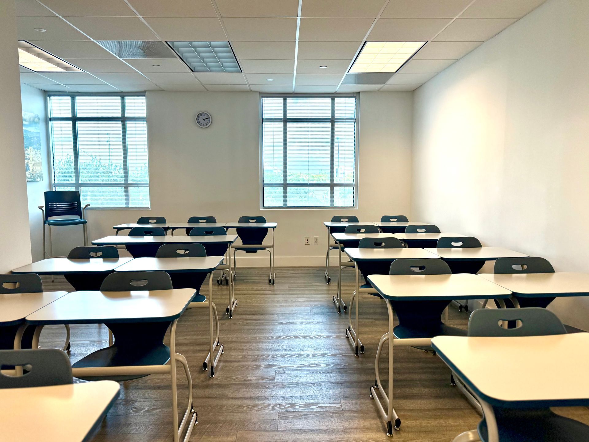 Empty classroom with rows of desks, large windows, and fluorescent ceiling lights.
